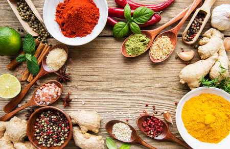 A selection of various colorful spices on a wooden table in bowls and spoonsの写真素材