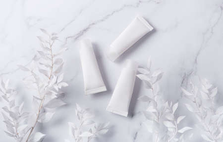 White tubes of cream on a marble background and decorative branch with white leavesの写真素材