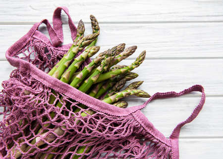 Asparagus stems in an eco mesh bag on a old wooden backgroundの写真素材