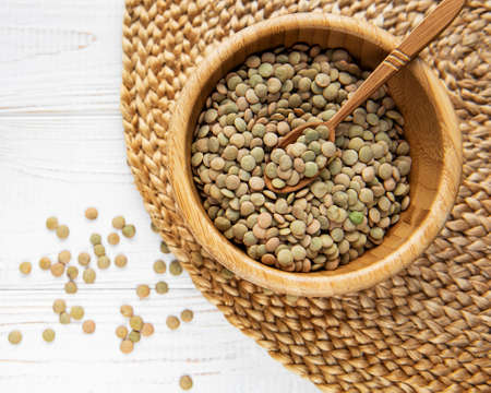 Pile of raw lentil in a bowl on white wooden background