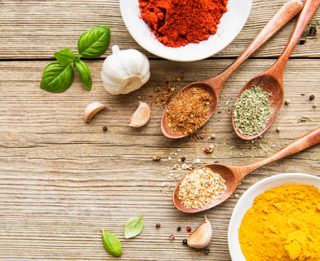 A selection of various colorful spices on a wooden table in bowls and spoonsの写真素材