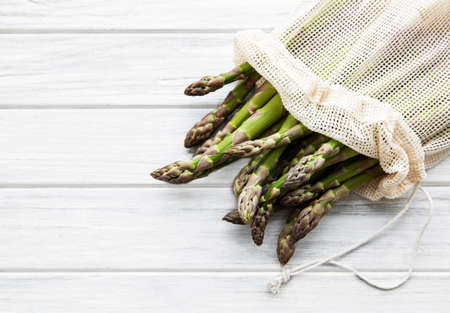Asparagus stems in an eco mesh bag on a old wooden backgroundの写真素材