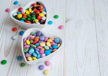 Heartshaped bowls with multicolored dragee sweets on a wooden backgroundの写真素材
