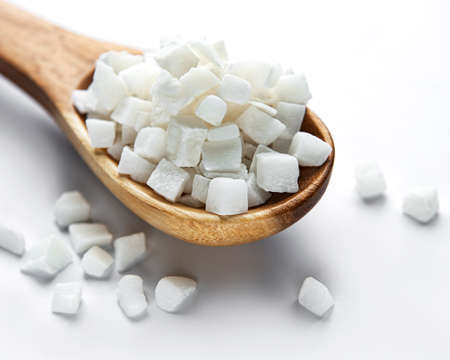 Dried sweet coconut cubes in spoon on white background.