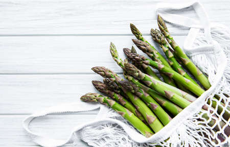 Asparagus stems in an eco mesh bag on a old wooden backgroundの写真素材