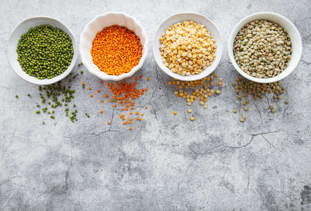 Bowls with different types of legumes on a gray concrete background