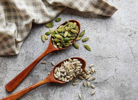 Wooden spoons with sunflower seeds and pumpkin seeds on a gray concrete background