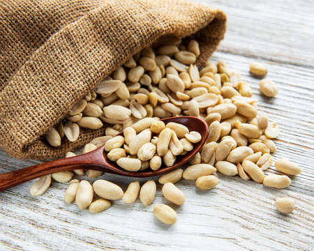 Peeled peanuts in a burlap bag on a white wooden backgroundの写真素材