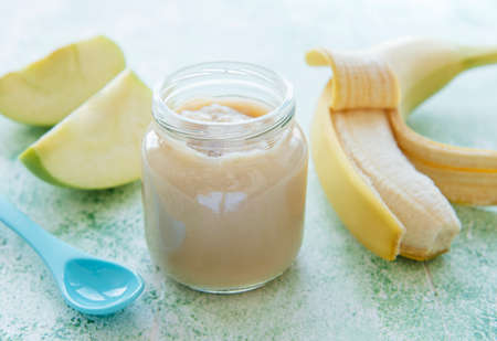 Jar of banana puree, apples and banana on green wooden tableの写真素材