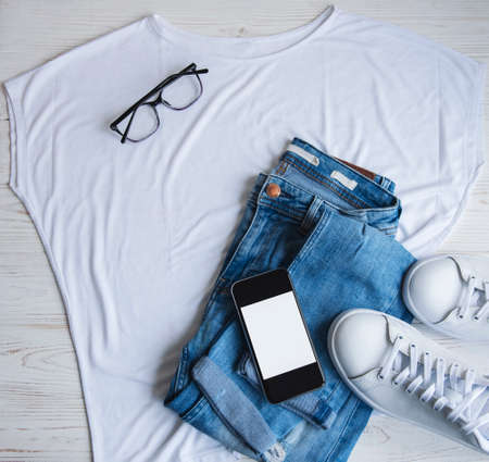 Stylish female clothes set. Woman outfit on wooden background. Blue jeans, white t-shirt, white sneakers and sunglasses. Flat lay, top viewの写真素材