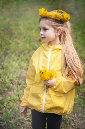 Little girl with a wreath of yellow dandelions on her headの写真素材