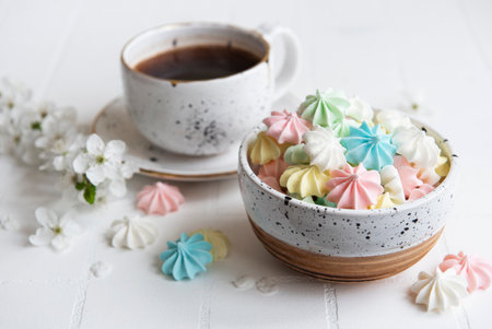 Cup with coffee and small meringues in the bowl on a tiled background