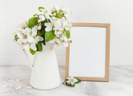 Spring apple blossom in a vase with an empty photo frame on the tableの写真素材