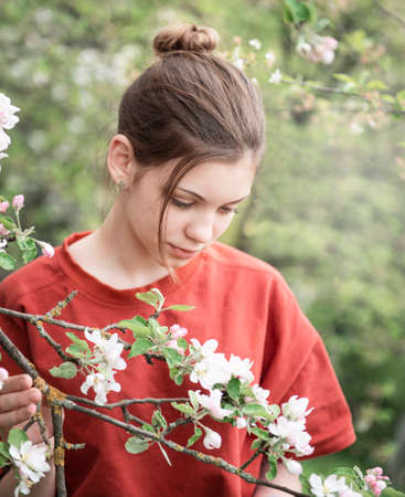 A young girl in a blooming garden looks at flowering trees