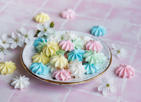 Small colorful meringues in the ceramic plate on pink tile background