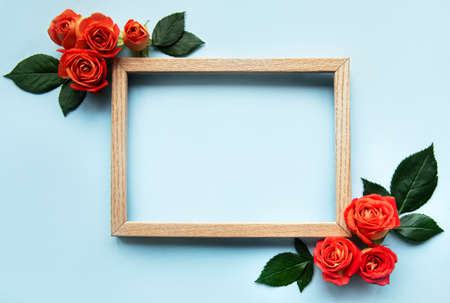 Flowers composition. Wooden frame and red roses and leaves on blue background. Top view, flat lay,...