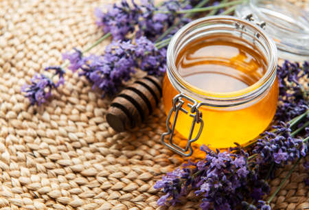 Jar with honey and fresh lavender flowers on a straw mat