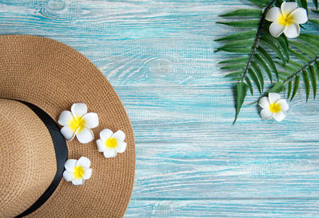 Summer vacation concept. Straw hat and frangipani flowers on blue wooden background