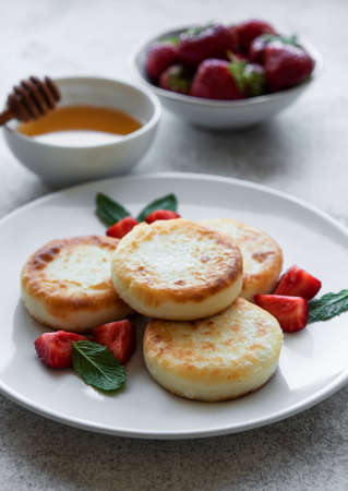 Cottage cheese pancakes, ricotta fritters on ceramic plate with fresh strawberry. Healthy and delicious morning breakfast. Gray concrete background.の写真素材