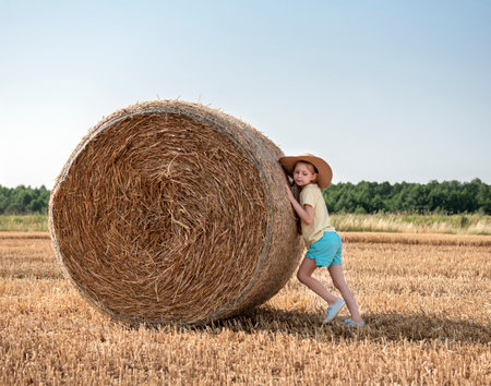 Little girl having fun in a wheat field on a summer day. Child playing at hay bale field during harvest time.の写真素材