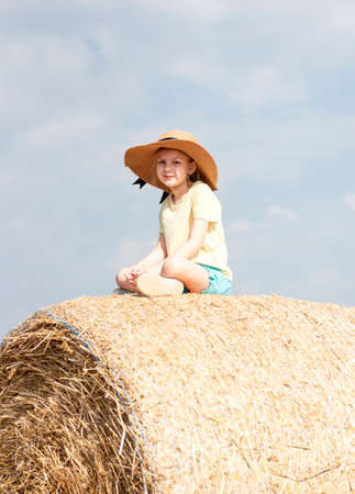 Little girl having fun in a wheat field on a summer day. Child playing at hay bale field during harvest time.の写真素材