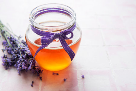 Jar with honey and fresh lavender flowers on a tile backgroundの写真素材