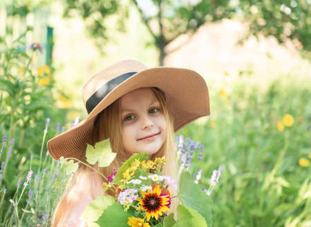 Little girl in a straw hat surrounded by lavender flowers. Portrait of the happy little girl blonde with long hair in lavender fieldの写真素材