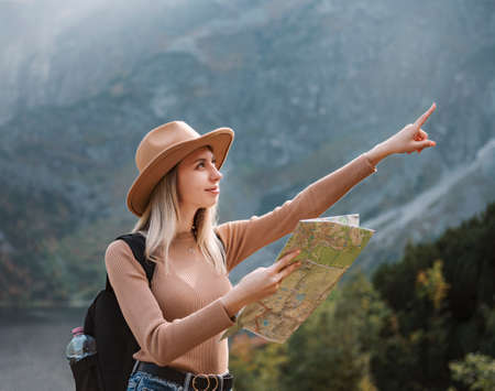 Wanderlust and travel concept. Stylish traveler girl in hat looking at map, exploring woods. Young...