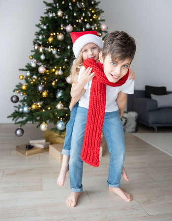 Children - a boy and a girl are playing near the Christmas tree. Living room interior with Christmas tree and decorations. New Year. Gift giving.の写真素材