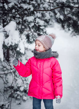 A little girl in a bright jacket plays in the winter snowy forest.の写真素材