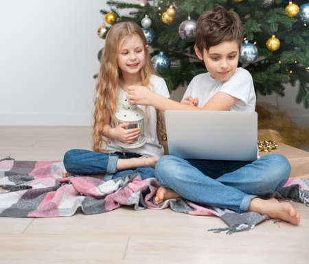 Christmas tree in a large living room. Children play near the Christmas tree. A boy with a laptop communicates with friends.の写真素材