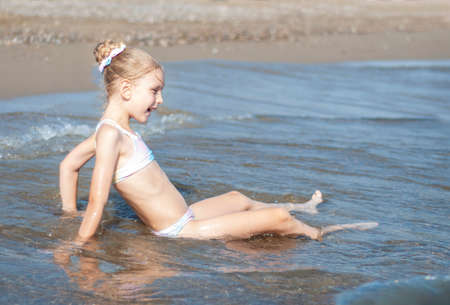 Little girl in a bathing suit playing on the beach by the seaの写真素材