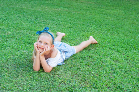 Ð¡heerful little girl in a denim jumpsuit, lying on a green grassの写真素材