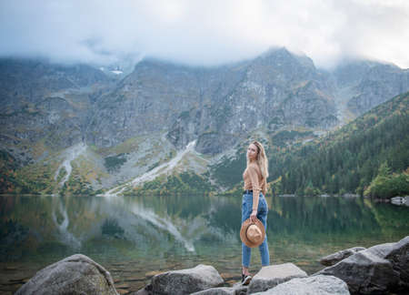 Wanderlust and travel concept. Stylish traveler girl in hat. Young woman with backpack traveling at lake in forest.の写真素材