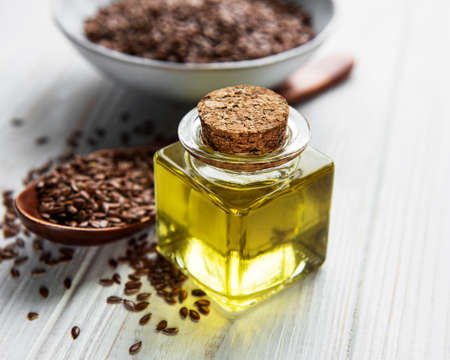Flax seeds or linseeds in spoon and bowl with glass of linseed oil on wooden backdropの写真素材