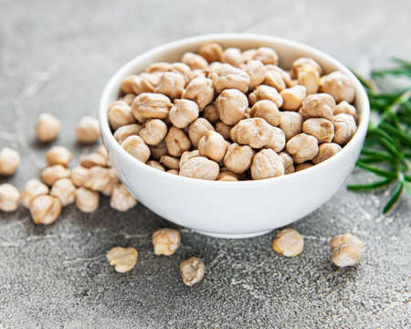 Uncooked dried chickpeas in bowl on a gray concrete background