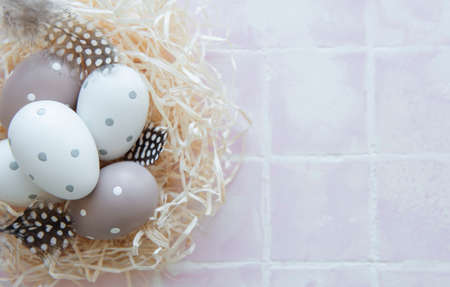 Easter eggs in straw nest on a pink tile background