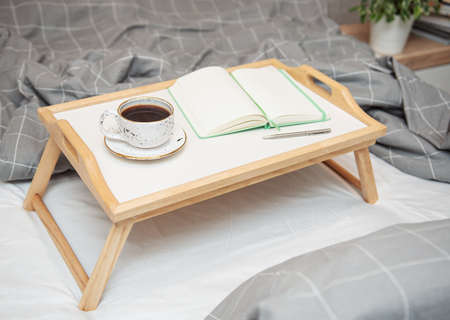 Breakfast in bed. Coffee and notebook on a wooden tray. Work at home concept.