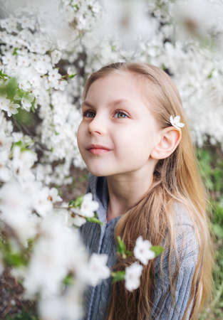 Cute child with blond hair in a blooming garden