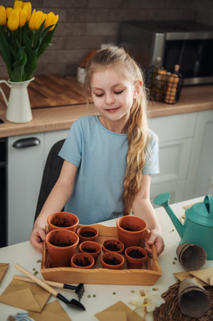 Little girl sitting at the table at home, sowing seeds into flower pots. home gardening