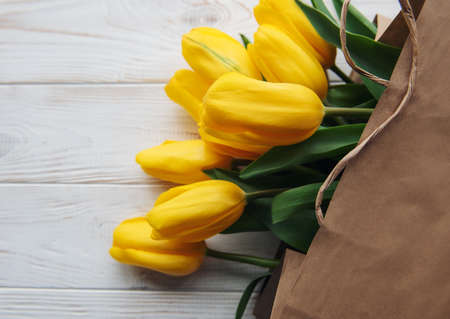 Bouquet of yellow tulips in a kraft paper bag on a white wooden backgroundの写真素材