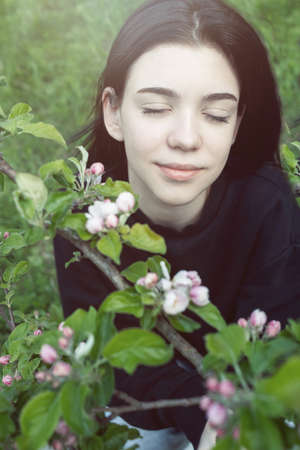 Pretty teen girl are posing in garden near blossom apple tree with pink flowers. spring timeの写真素材