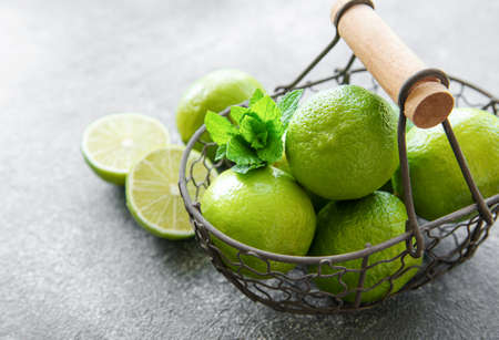 Green  Limes with fresh mint leaves in basket, concrete backgroundの写真素材