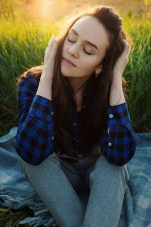 Portrait of a beautiful young woman on meadow watching the sunset enjoying nature summer evening...