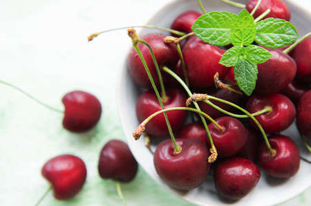 Fresh red cherries fruit in bowl on a green wooden background