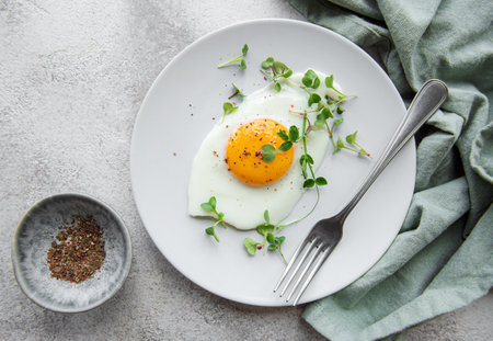 Fried eggs, microgreens and spices on a white plate on concrete background