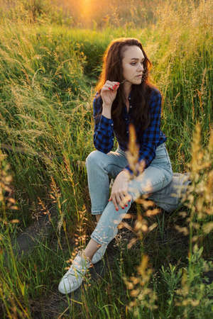 Portrait of a beautiful young woman on meadow watching the sunset enjoying nature summer evening...