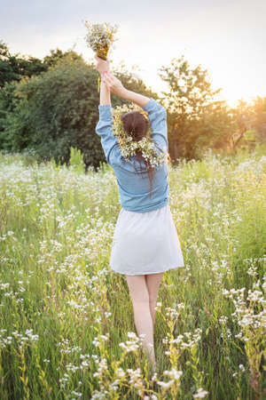 Beautiful young woman holding wildflowers bouquet and  walking in flower field on sunset.の写真素材
