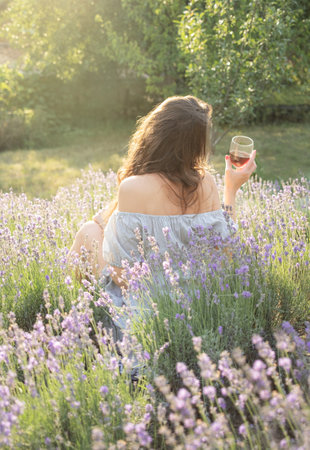 Beautiful girl is drinking  wine in lavender fieldの写真素材