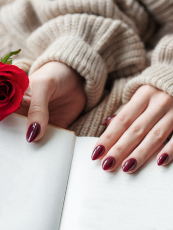 Beautiful hands of a young woman with dark red manicure on nails. Autumn concept. Hands of a girl in a warm brown sweater leafing through a bookの写真素材